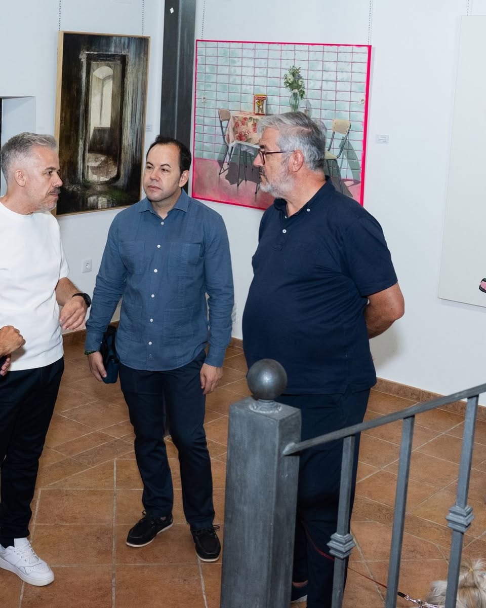 Tres visitantes conversan ante las obras del certamen de pintura